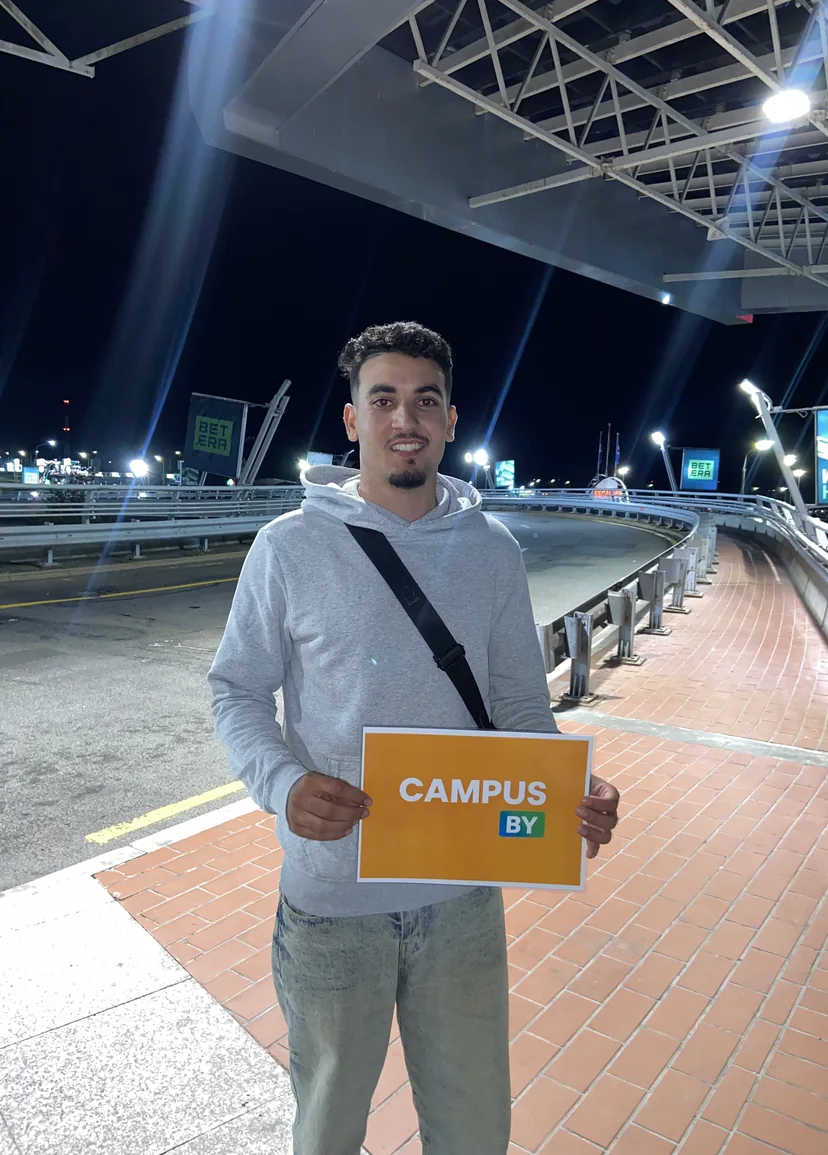 Étudiant accueilli à l'aéroport de Minsk, tenant le panneau Campus By